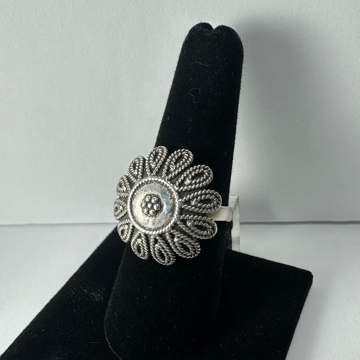 Silver ring with an intricate flower design featuring looped petals and a beaded center, displayed on a black velvet finger stand.