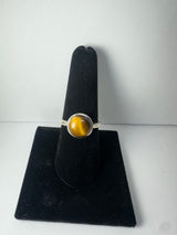 Silver ring with a round tiger's eye stone displaying golden and brown hues, presented on a black velvet ring stand against a plain white background.