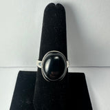 Silver ring with a large polished black onyx oval stone mounted vertically on a black velvet finger display against a neutral background.