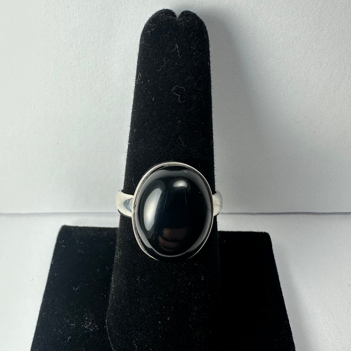 Silver ring with a large polished black onyx oval stone mounted vertically on a black velvet finger display against a neutral background.
