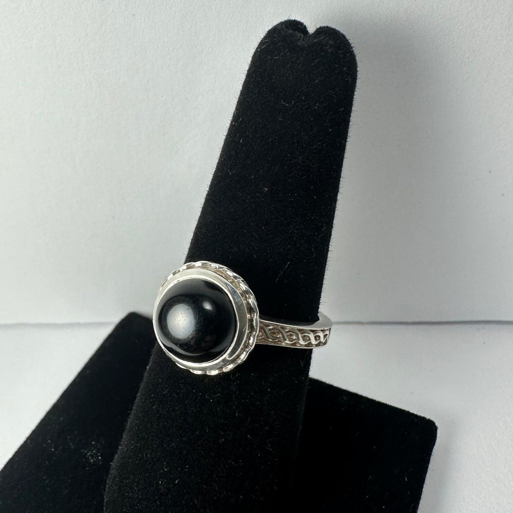 Silver ring with a round black onyx stone set in a decorative bezel, displayed on a black velvet ring holder against a plain white background.