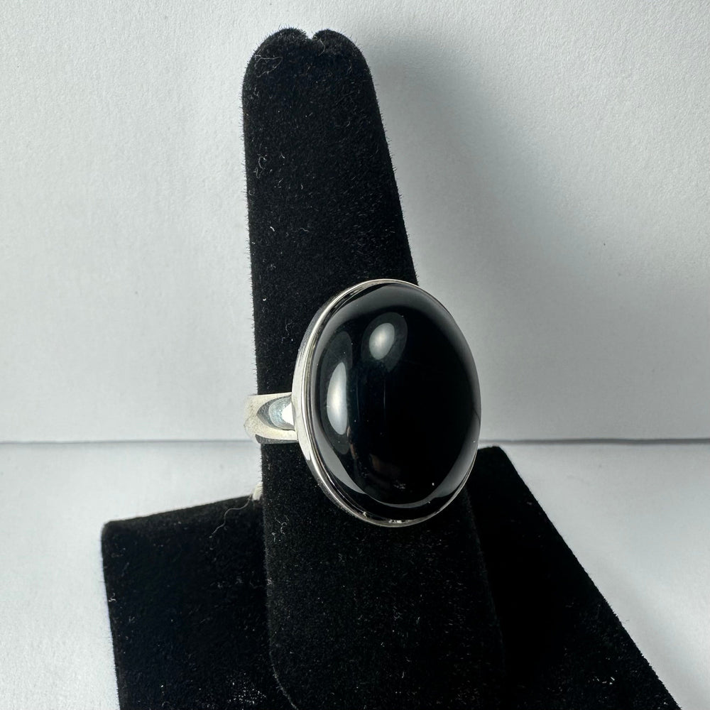 Silver ring with a large, smooth oval black onyx stone set in a simple bezel setting, displayed on a black velvet finger stand against a plain background.