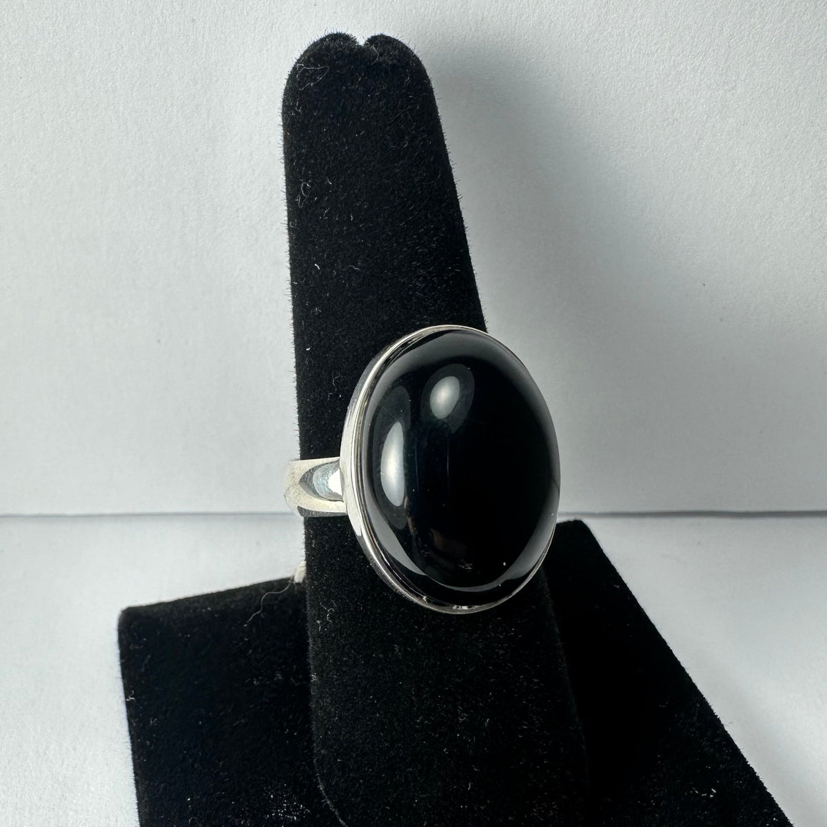 Silver ring with a large, smooth oval black onyx stone set in a simple bezel setting, displayed on a black velvet finger stand against a plain background.