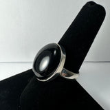 Silver ring with a large polished black onyx stone set in a smooth bezel, displayed on a black velvet finger stand against a plain white background.