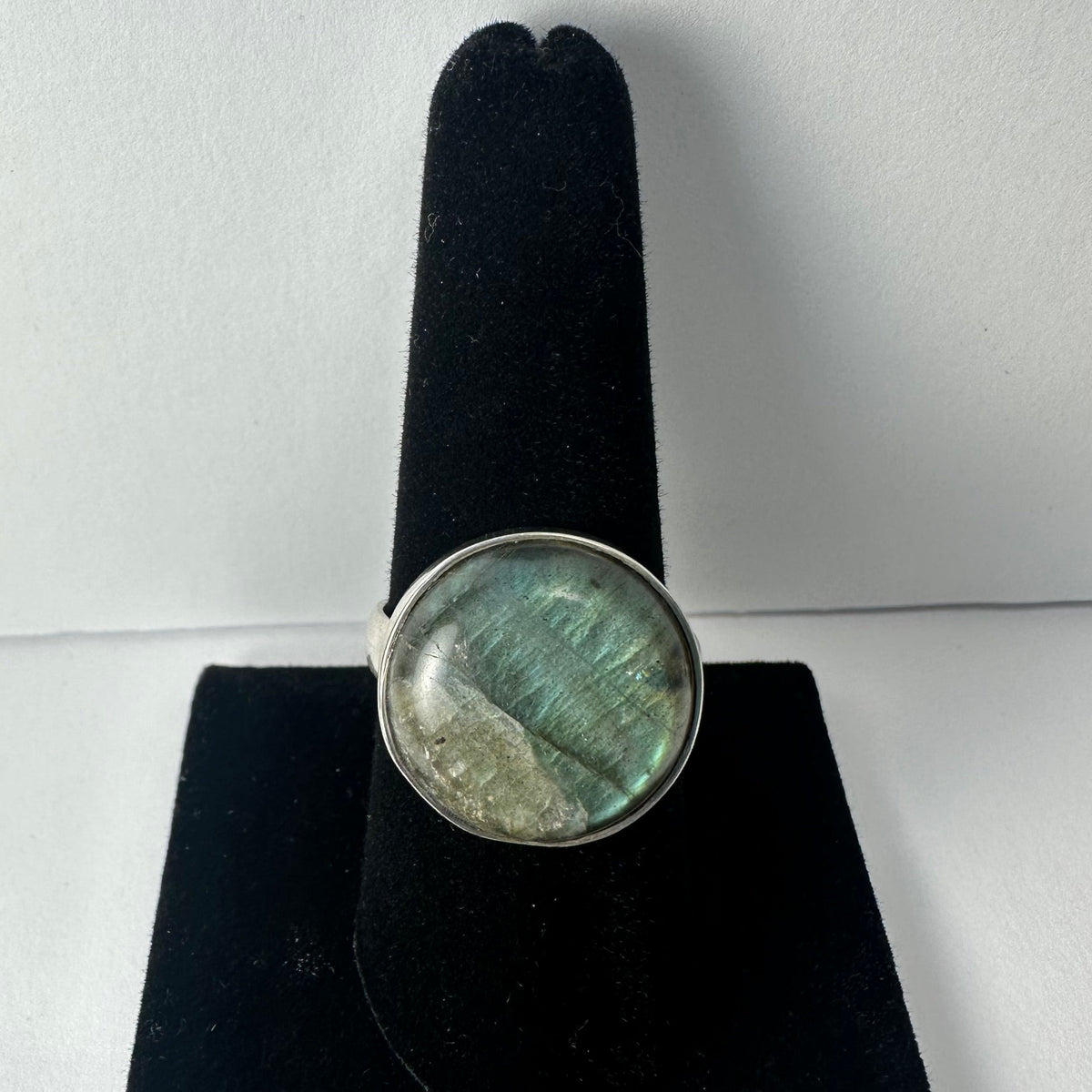 Round labradorite ring with green and blue iridescent hues set in a simple silver band, displayed on a black velvet ring holder.