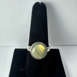 Silver ring with a round labradorite stone showing green and gold iridescence set on a black velvet ring display.