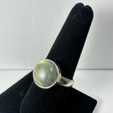 Silver ring with a polished oval labradorite gemstone showing green and yellow reflections, displayed upright on a black velvet ring holder.