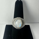 Oval moonstone set in a wide silver band with a geometric hexagonal pattern, displayed on a black velvet ring stand against a neutral background.