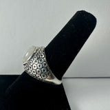 Silver ring with a rounded moonstone cabochon on top, featuring a textured geometric pattern on the band, displayed on a black velvet ring holder.