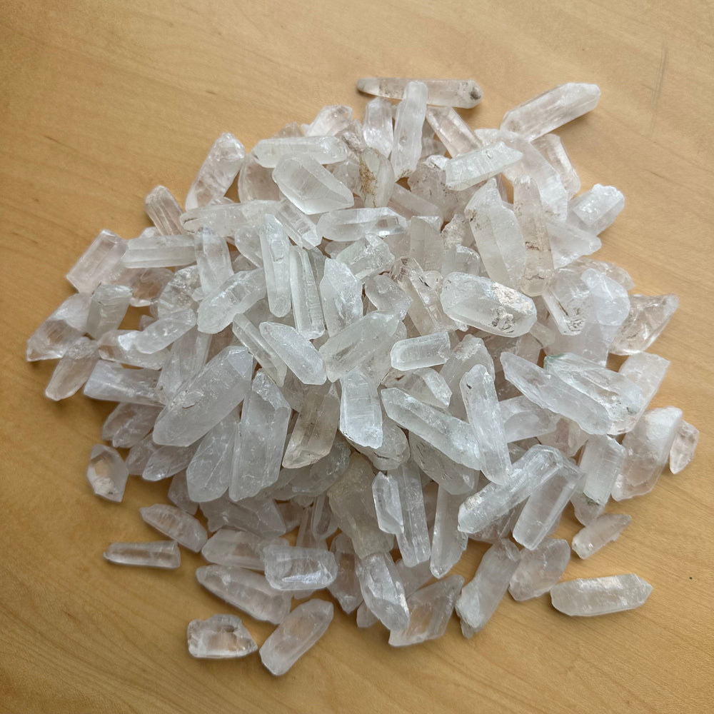 Cluster of translucent Brazilian quartz crystal points with natural facets and slight color variations, resting on a light wood surface.