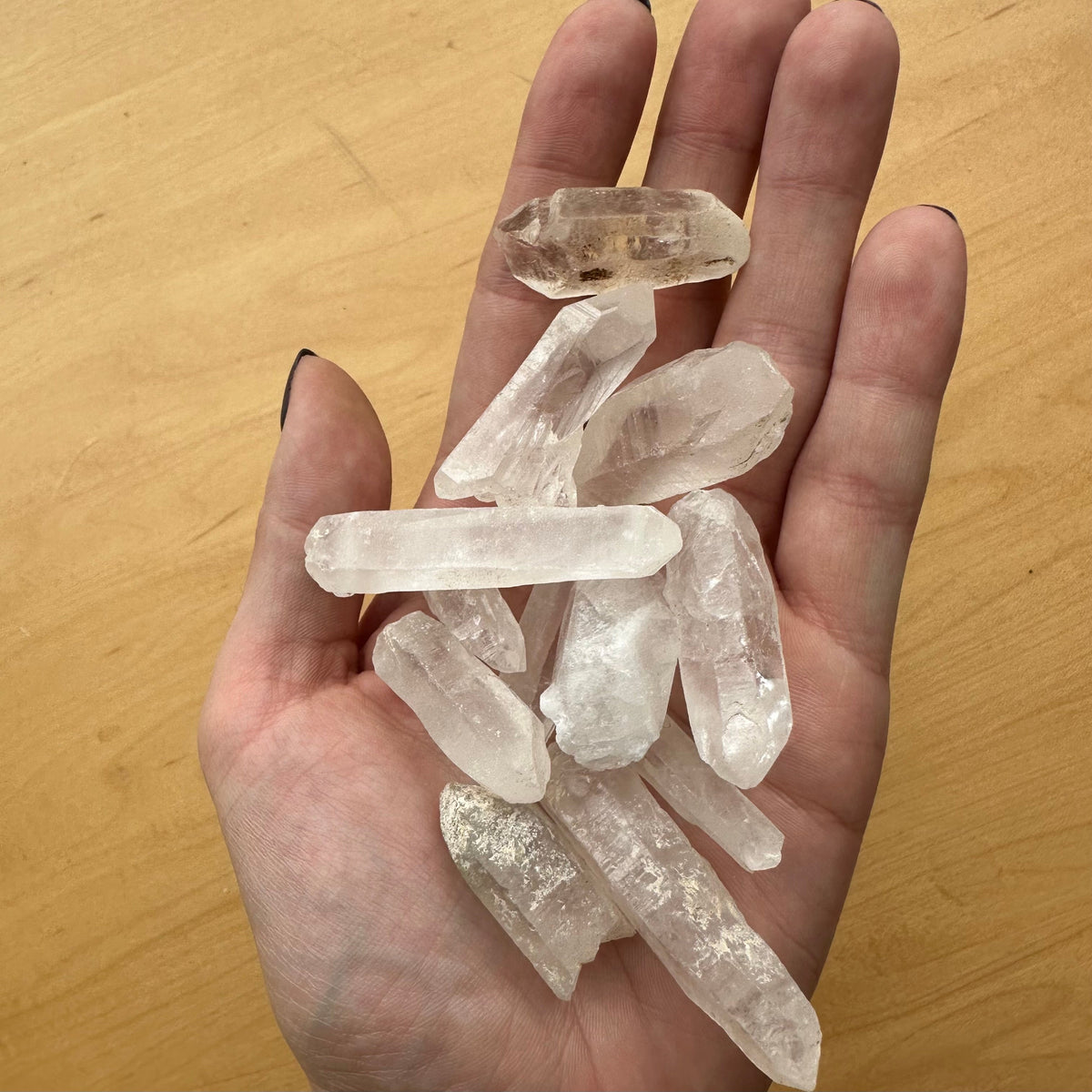 Hand holding several translucent, irregularly shaped Brazilian quartz crystal points with varying clarity and some included veining.