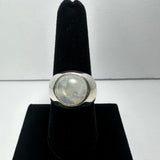 Silver ring with a round, translucent moonstone cabochon set in the center, displayed on a black velvet finger stand against a plain background.