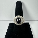 Silver ring with a large oval garnet cabochon set in a textured band, displayed upright on a black velvet ring holder against a plain white background.