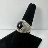 Silver ring with a smooth, domed dark red garnet stone set in a textured band featuring a bubble-like pattern, displayed on a black velvet ring stand.
