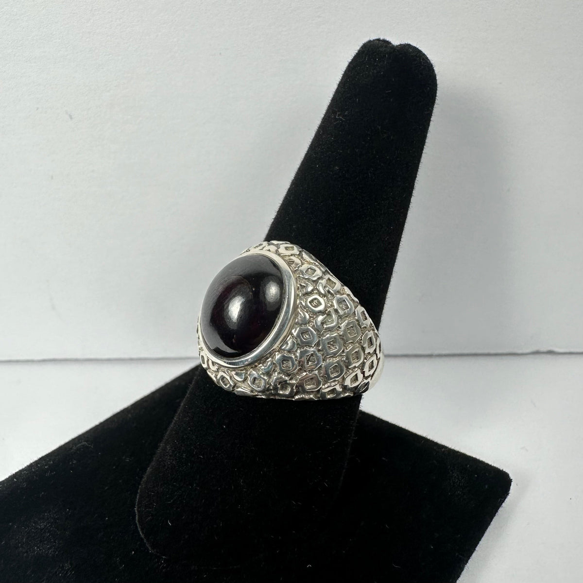 Silver ring with a smooth, domed dark red garnet stone set in a textured band featuring a bubble-like pattern, displayed on a black velvet ring stand.