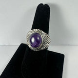 Silver ring with a domed amethyst stone in the center, set on a textured band with a repeating circular pattern, displayed on a black velvet stand.