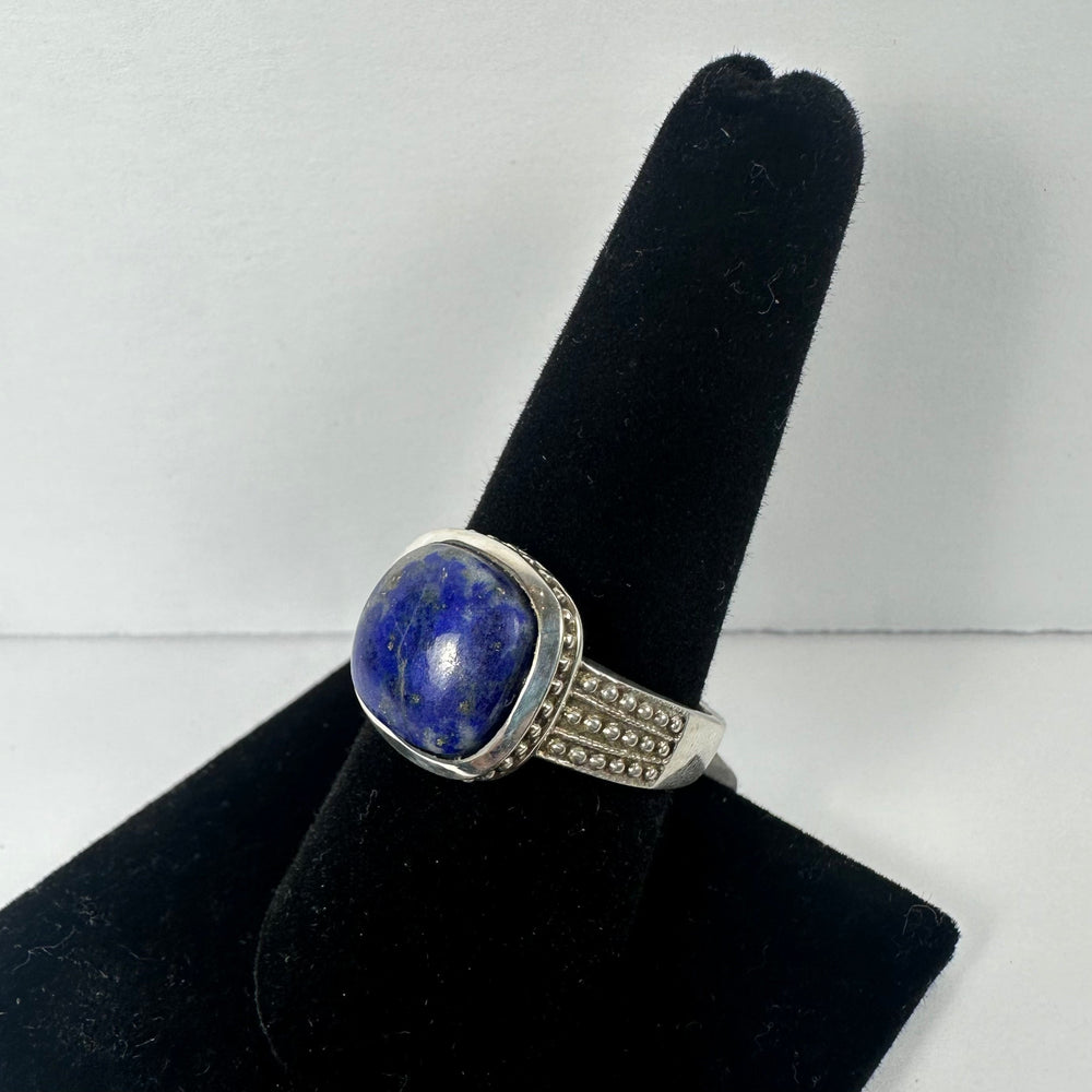 Silver ring with a polished lapis lazuli cabochon and beaded detailing along the band, displayed on a black velvet ring holder.