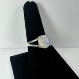 Silver ring with a round moonstone featuring a subtle blue flash, displayed on a black velvet finger-shaped stand against a plain background.