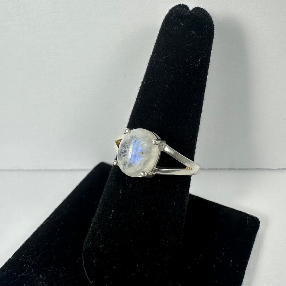Silver ring with an oval moonstone displaying blue iridescence, set in a split-shank band, shown on a black velvet finger stand against a plain background.