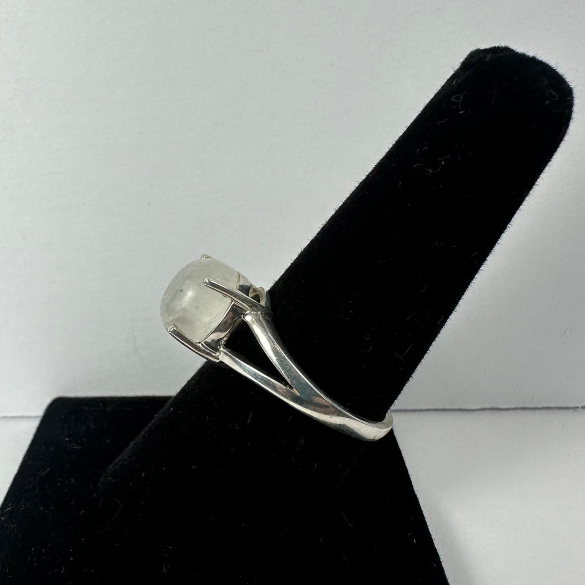 Silver ring with a smooth, translucent moonstone set in a four-prong setting, displayed on a black velvet ring holder against a plain background.