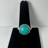Silver ring with a smooth, round turquoise stone set in a simple bezel, displayed upright on a black velvet ring holder against a white background.