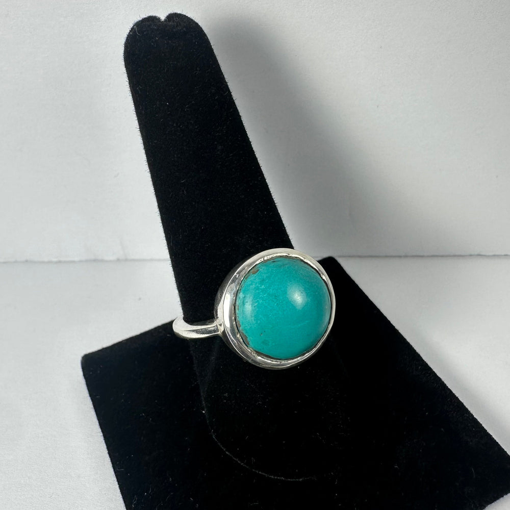 Silver ring with a large round turquoise stone, displayed on a black velvet ring holder against a plain light background.