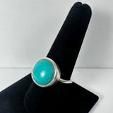 Silver ring with a smooth, round turquoise stone set in a simple bezel band, displayed on a black velvet ring holder.