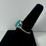 Silver ring with round turquoise stone set in bezel, displayed on black velvet ring stand against white background