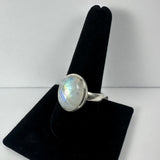 Oval moonstone set in a simple silver bezel ring displayed on a black velvet ring holder against a white background.