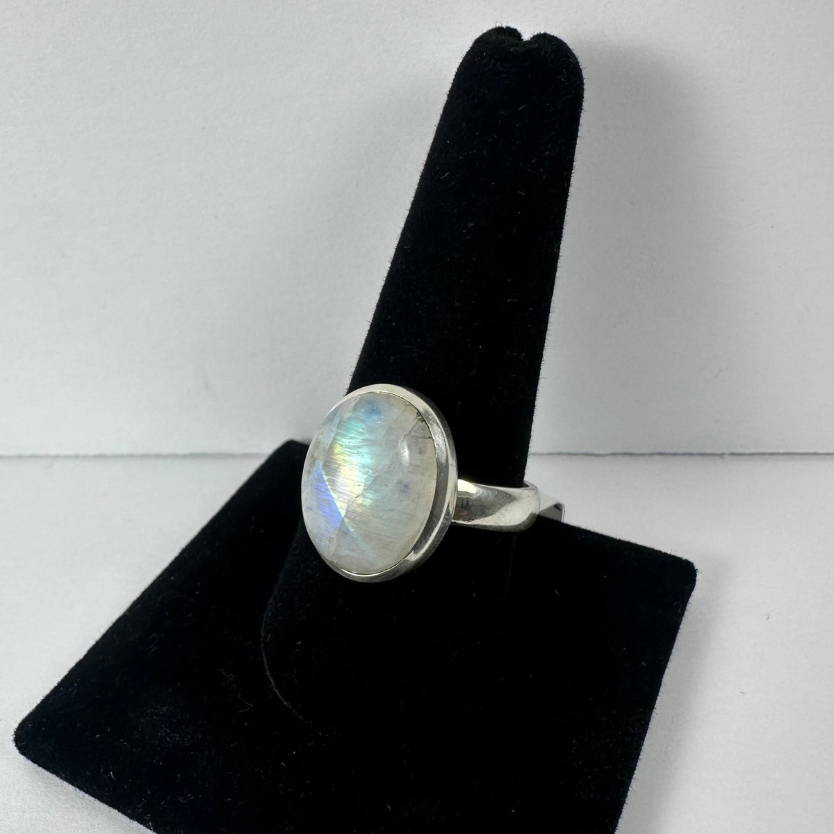 Oval moonstone set in a simple silver bezel ring displayed on a black velvet ring holder against a white background.