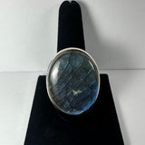 Oval labradorite ring with blue and gray iridescent facets set in a simple silver bezel on a black velvet display stand.