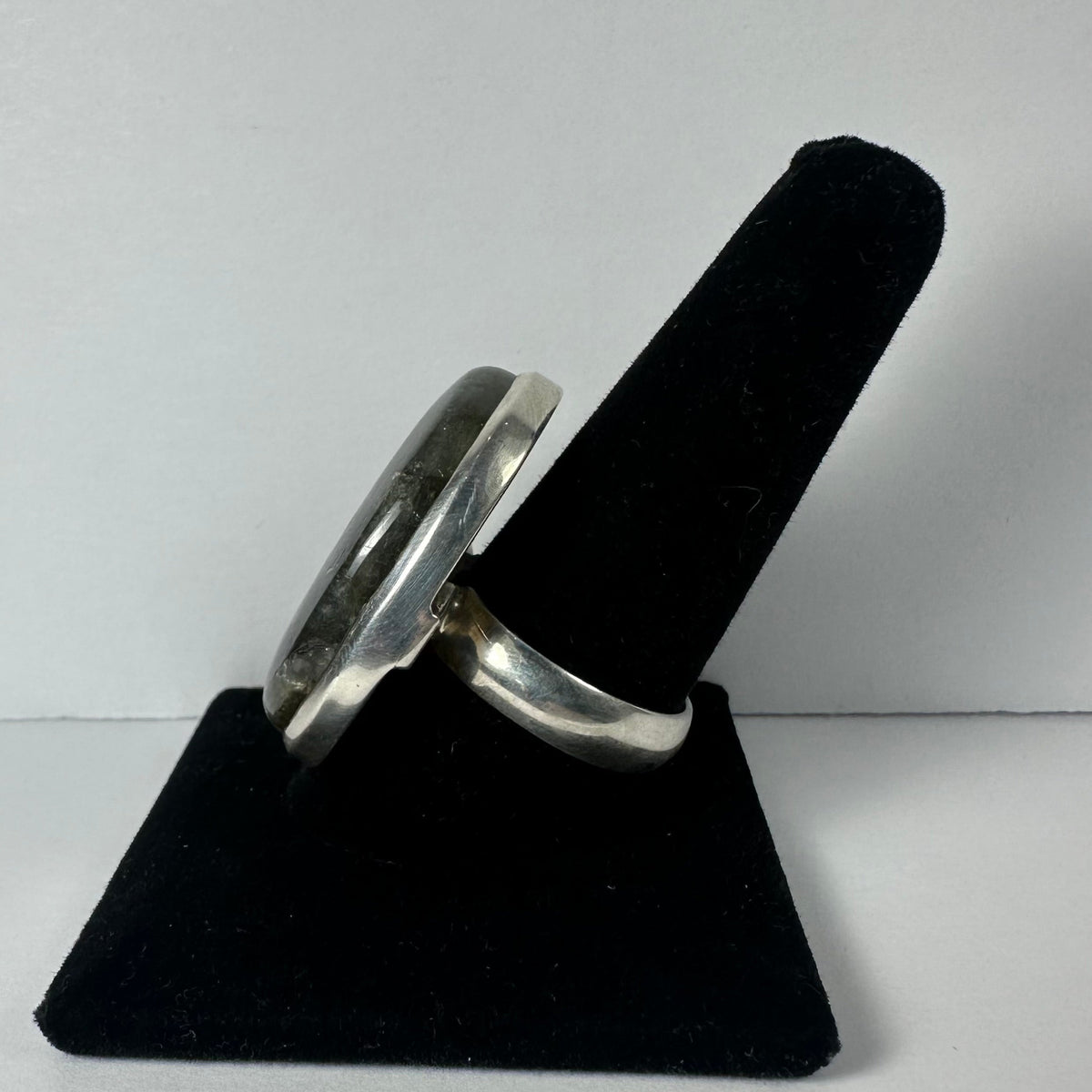 Silver ring with an oval labradorite stone set in a simple bezel, displayed on a black velvet finger stand against a plain white background.