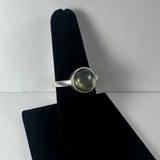 Silver ring with a round labradorite stone displaying subtle green and gray tones, shown on a black velvet ring display stand against a white background.