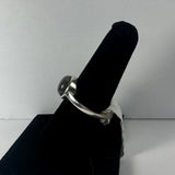 Silver ring with a rounded, polished labradorite stone set in a simple bezel, displayed on a black velvet ring holder against a white background.