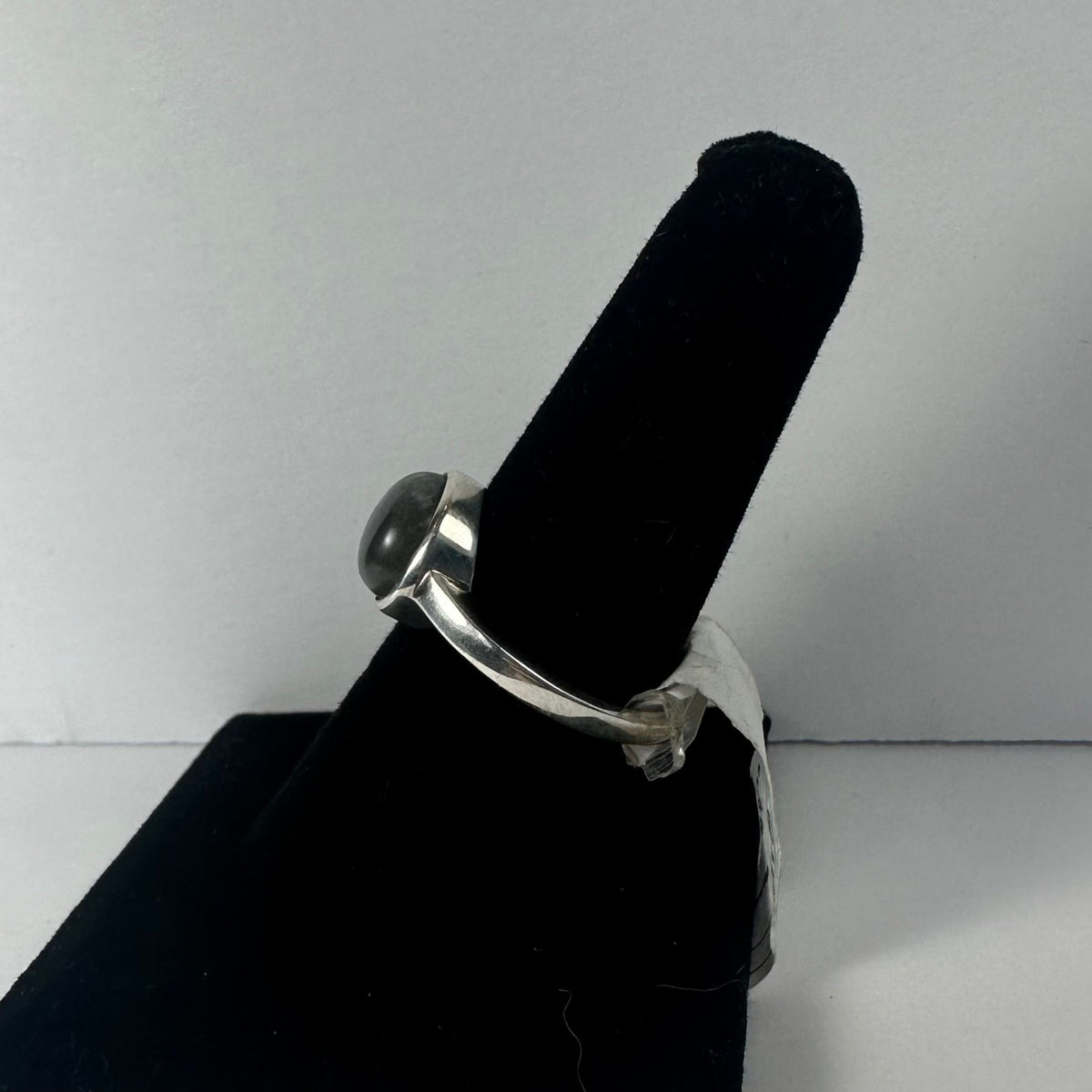 Silver ring with a rounded, polished labradorite stone set in a simple bezel, displayed on a black velvet ring holder against a white background.