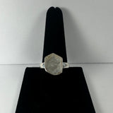 Silver ring with a natural rough hexagonal quartz stone set on a black velvet display against a plain light gray background.