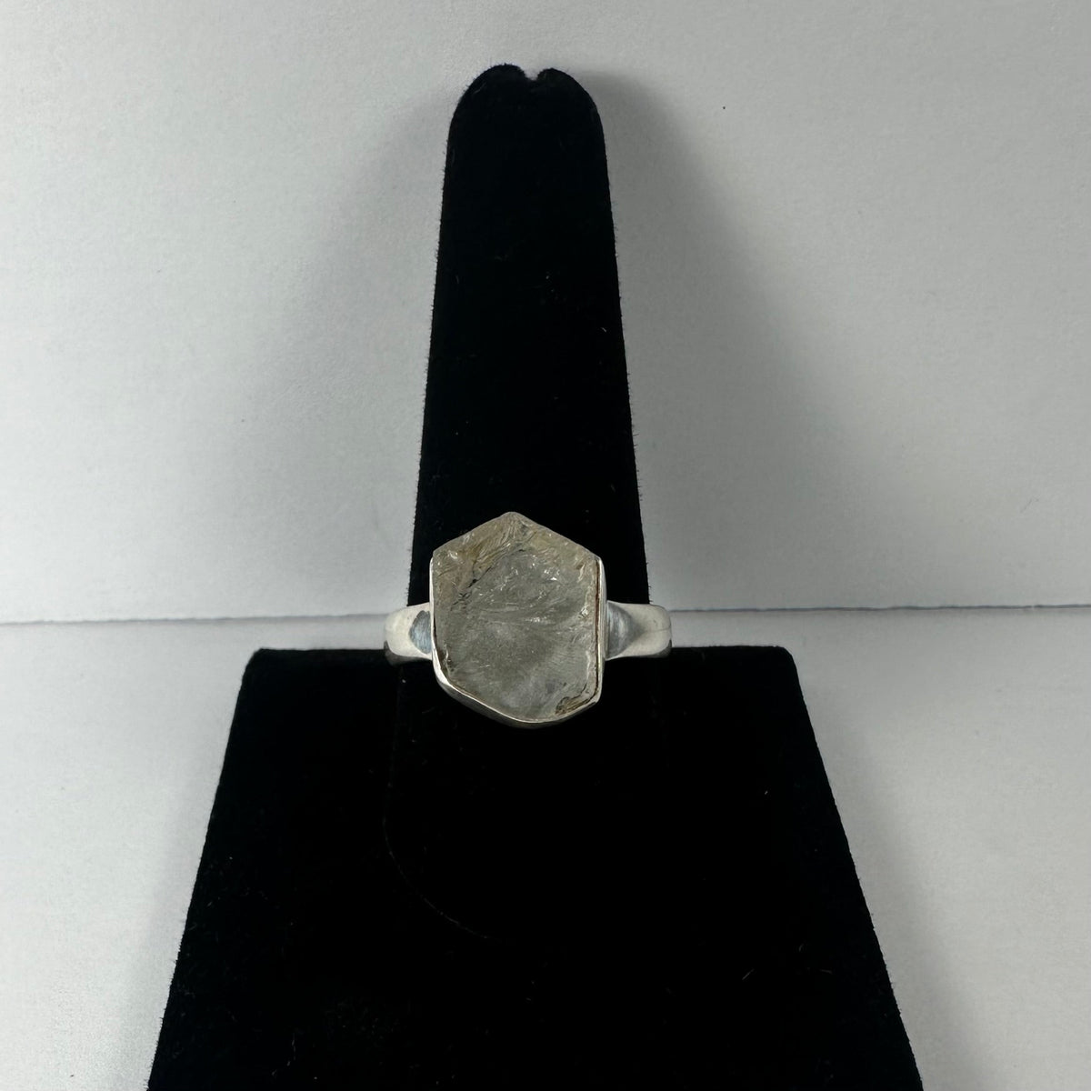Silver ring with a natural rough hexagonal quartz stone set on a black velvet display against a plain light gray background.