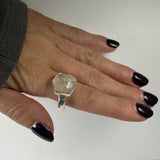 Hand with dark purple nails wearing a silver ring featuring a large, irregularly shaped natural rough quartz stone on the middle finger.