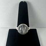 Round clear moonstone cabochon with internal inclusions set in a simple silver band displayed on a black velvet ring holder.