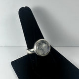 Silver ring with a rounded bezel setting featuring a cloudy, translucent moonstone, displayed on a black velvet ring holder against a light background.