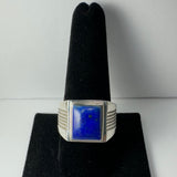 Silver ring with a rectangular deep blue lapis lazuli stone, featuring subtle gold flecks, displayed on a black velvet ring holder.