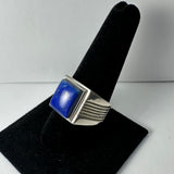 Silver ring with a polished square lapis lazuli stone set in a simple bezel, displayed on a black velvet ring stand showing a side view with ribbed band details.