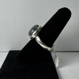 Silver ring with a smooth, rounded labradorite stone set in a bezel, displayed on a black velvet ring stand against a plain background.