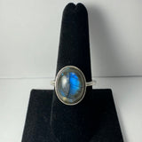Silver ring with an oval labradorite stone displaying blue and gray iridescence on a black velvet ring holder.