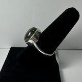 Silver ring with a polished gray labradorite stone set in a smooth bezel, displayed on a black velvet ring holder against a light background.