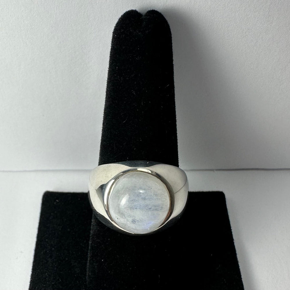 Polished silver ring with a round, translucent moonstone cabochon set in a bezel, displayed upright on a black velvet ring holder against a white background.