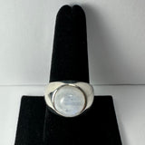 Polished silver ring with a round, translucent moonstone cabochon set in a bezel, displayed upright on a black velvet ring holder against a white background.