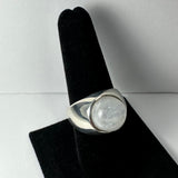 Rounded silver ring with a large, smooth, translucent moonstone mounted in a thick bezel, displayed upright on a black velvet stand