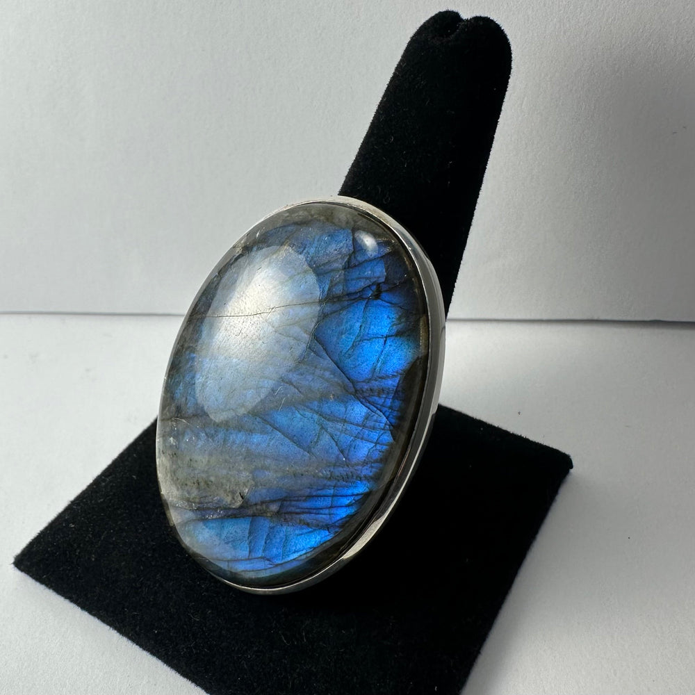 Oval labradorite ring with vibrant blue and gray iridescent flash set in a simple silver band, displayed on black velvet ring holder.