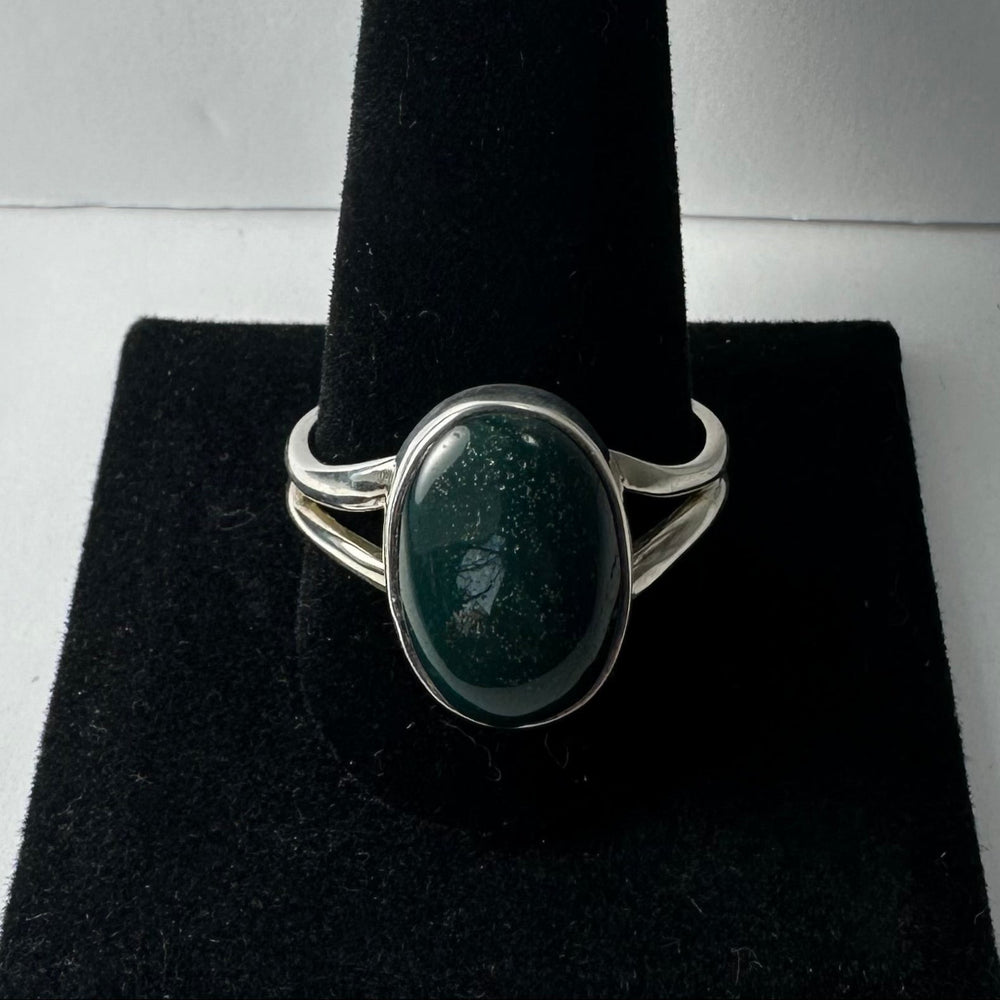 Silver ring with a polished dark green serpentine oval stone set in a split shank band, displayed on a black velvet ring holder.